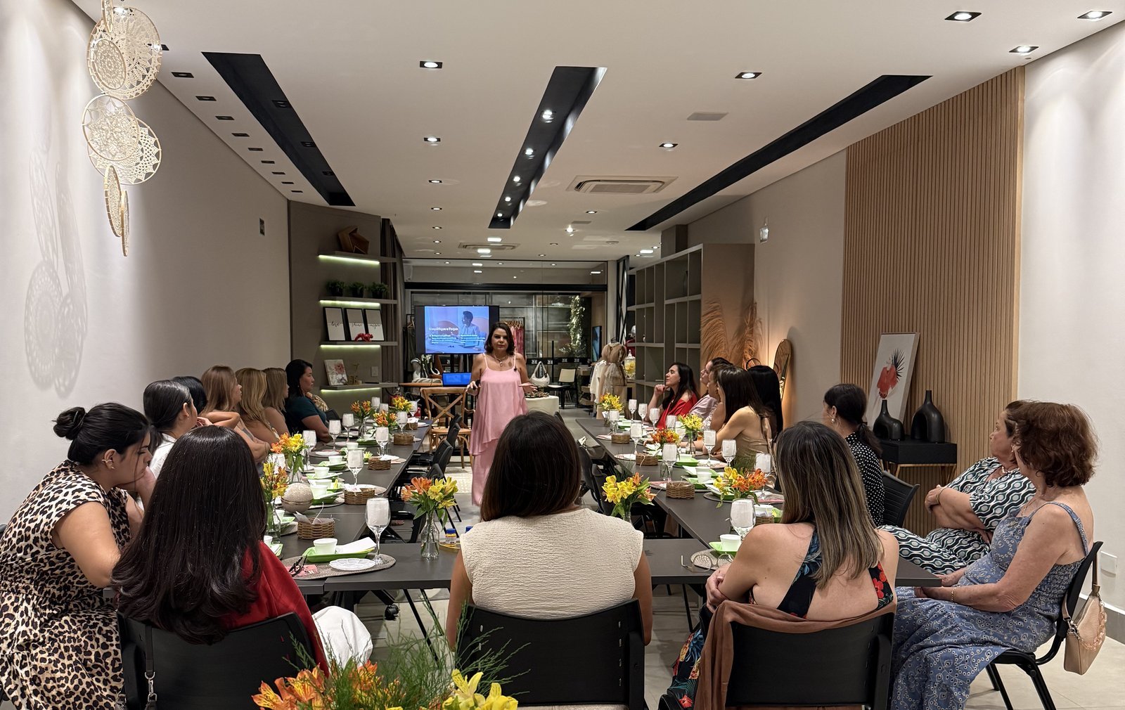 Val Dantas conduzindo um encontro presencial com uma sala cheia de mulheres